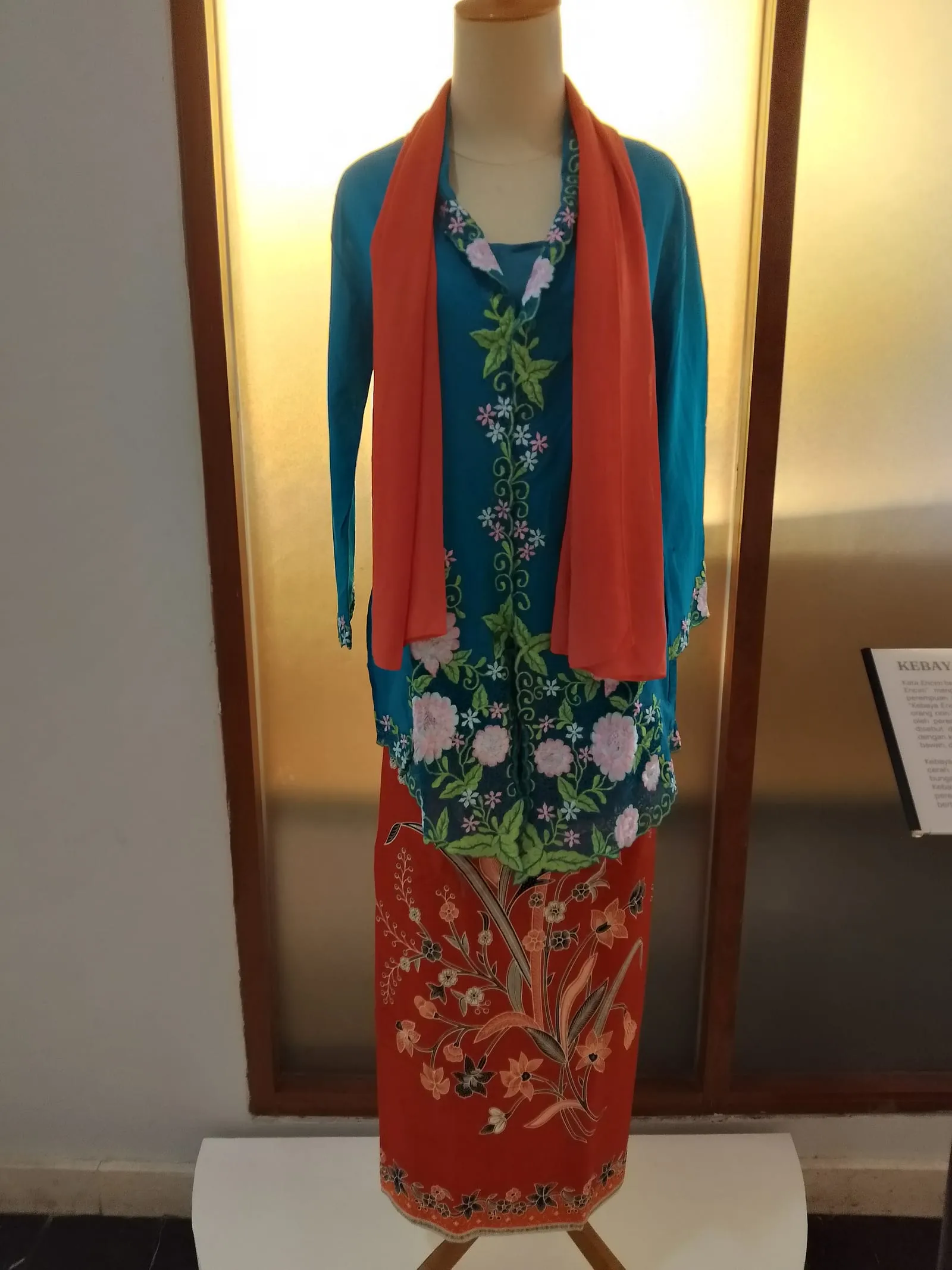 Kebaya nyonya biru berbordir bunga dengan selendang jingga